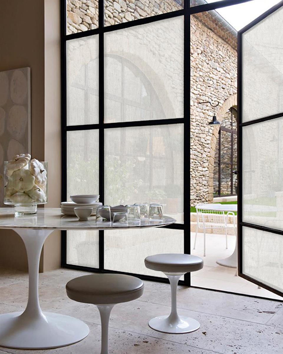 Store vinduer dekket med Squid vindutekstil, foran står et spisebord og stoler. Foto.